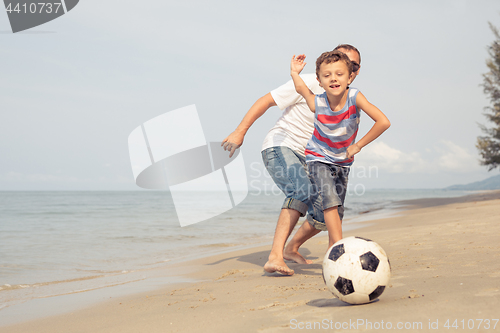 Image of Father and son playing football on the beach at the day time.