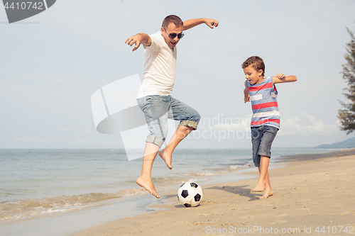 Image of Father and son playing football on the beach at the day time.