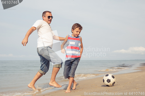 Image of Father and son playing football on the beach at the day time.