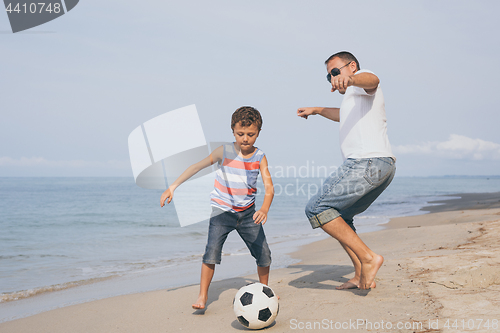 Image of Father and son playing football on the beach at the day time.