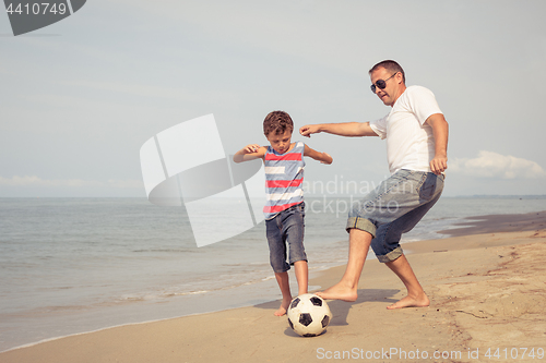 Image of Father and son playing football on the beach at the day time.