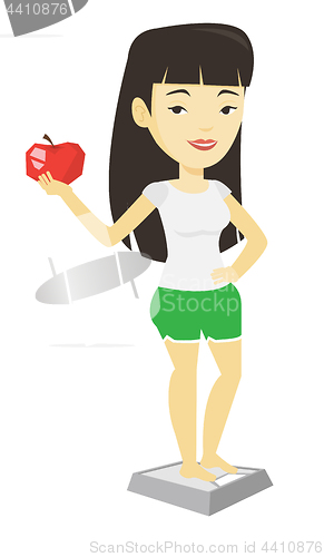 Image of Woman standing on scale and holding apple in hand.