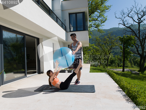 Image of woman and personal trainer doing exercise with pilates ball