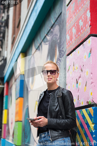 Image of Woman using smartphone against colorful graffiti wall in New York city, USA.