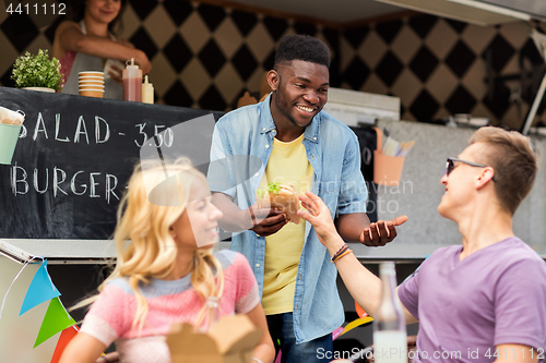 Image of happy friends with drinks eating at food truck