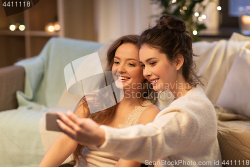 Image of female friends taking selfie by smartphone at home