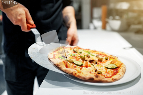 Image of cook with baked pizza on peel at pizzeria