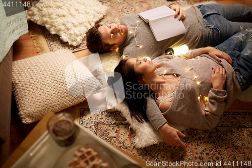 Image of happy couple with garland lying on floor at home