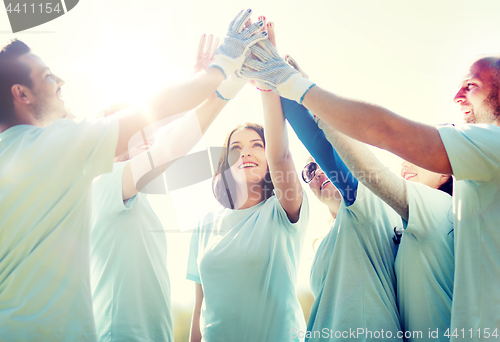 Image of group of happy volunteers making high five in park