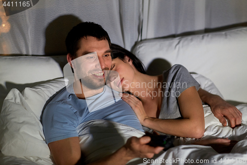 Image of happy couple watching tv in bed at night at home