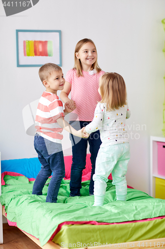 Image of happy little kids jumping on bed at home