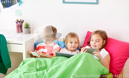 Image of kids with tablet pc and smartphones in bed at home