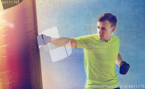 Image of young man in gloves boxing with punching bag