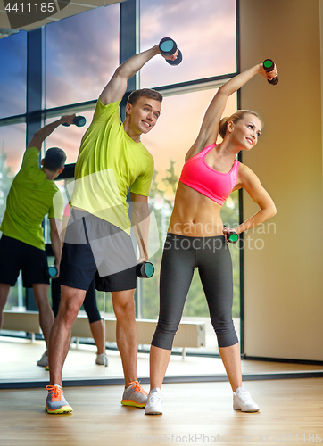 Image of smiling man and woman with dumbbells in gym