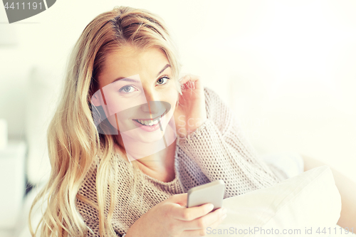 Image of happy young woman with smartphone in bed at home