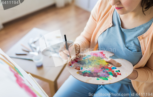 Image of artist with palette and brush painting at studio