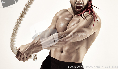 Image of Attractive muscular man working out with heavy ropes.