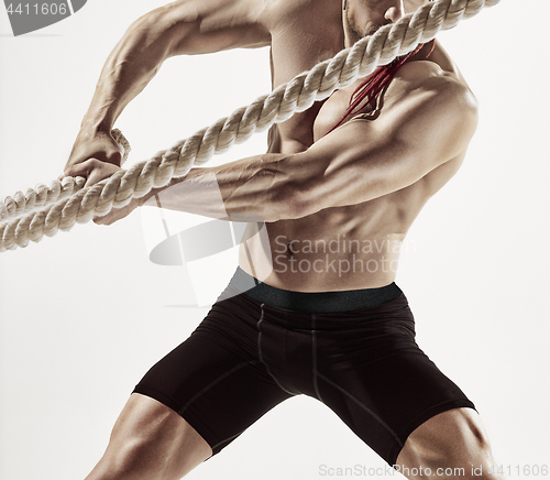 Image of Attractive muscular man working out with heavy ropes.