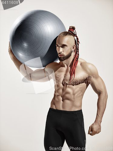 Image of Muscular man holding fitness ball, standing isolated on white