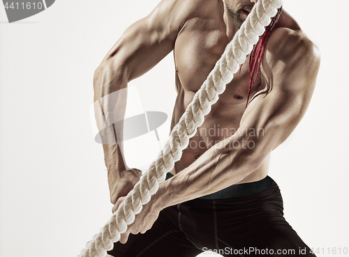 Image of Attractive muscular man working out with heavy ropes.