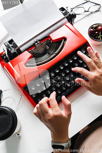 Image of Woman hand working with bright red vintage typewriter