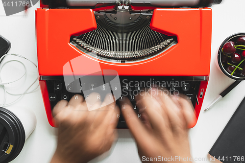 Image of Man hand working with bright red vintage typewriter