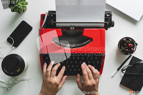 Image of Woman hand working with bright red vintage typewriter