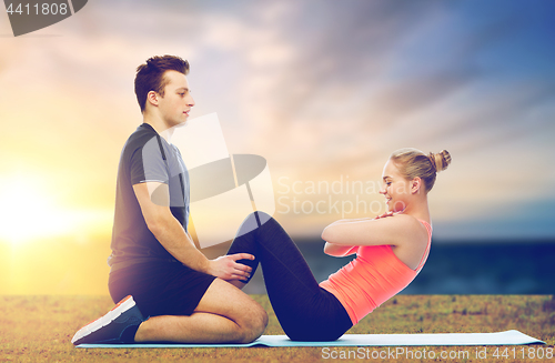 Image of happy sportive couple doing sit-ups outdoor