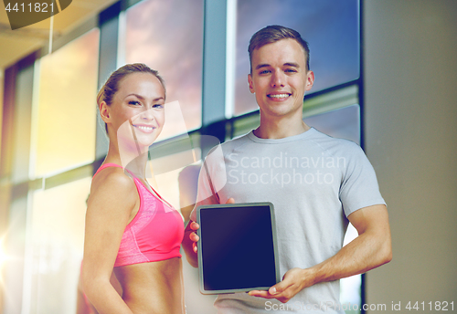 Image of smiling young woman with personal trainer in gym