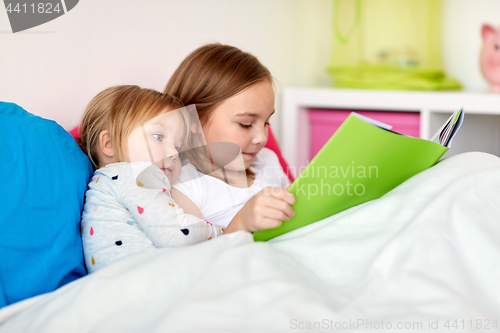 Image of little girls or sisters reading book in bed