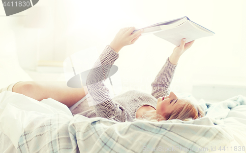 Image of young woman reading book in bed at home