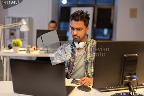 Image of creative man with laptop working at night office