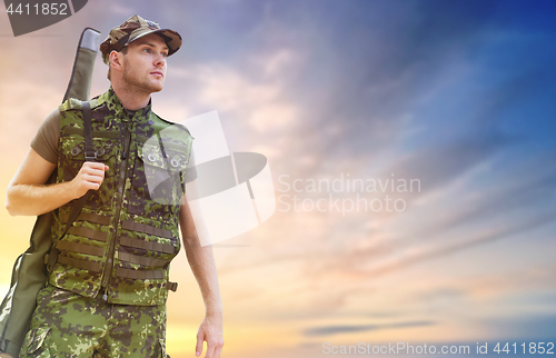 Image of young soldier or hunter with gun over sky