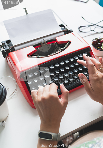 Image of Woman hand working with bright red vintage typewriter