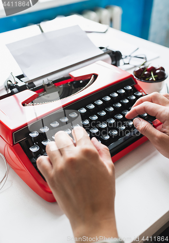 Image of Woman hand working with bright red vintage typewriter