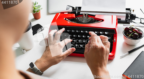 Image of Woman hand working with bright red vintage typewriter