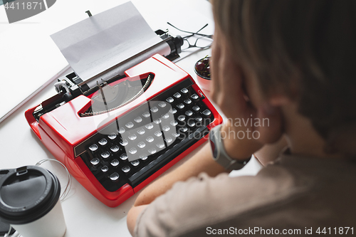 Image of Woman writer thoughtfully working on a book on her Desk red typewriter