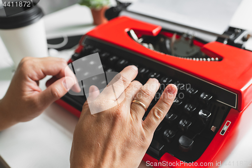 Image of Woman hand working with bright red vintage typewriter