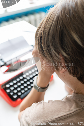 Image of Woman writer thoughtfully working on a book on her Desk red typewriter