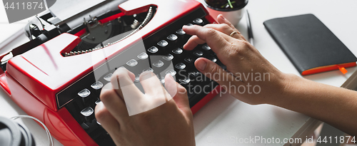 Image of Woman hand working with bright red vintage typewriter