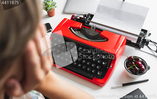 Image of Woman writer thoughtfully working on a book on her Desk red typewriter
