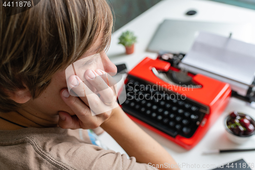 Image of Woman writer thoughtfully working on a book on her Desk red typewriter