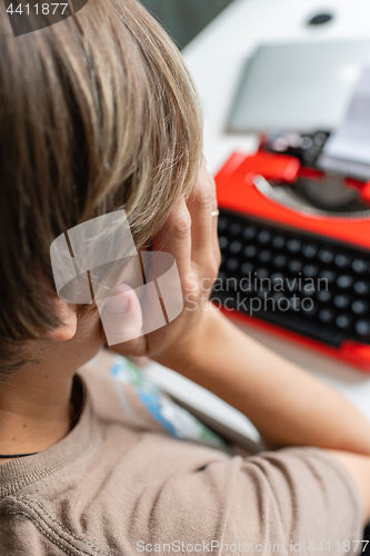 Image of Woman writer thoughtfully working on a book on her Desk red typewriter