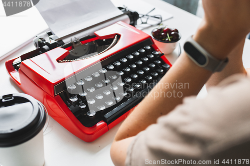 Image of Woman writer thoughtfully working on a book on her Desk red typewriter