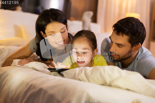 Image of family with tablet pc in bed at night at home