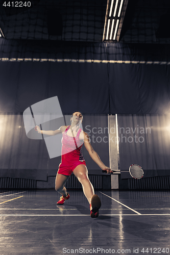 Image of Young woman playing badminton at gym