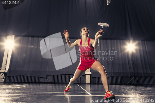 Image of Young woman playing badminton at gym