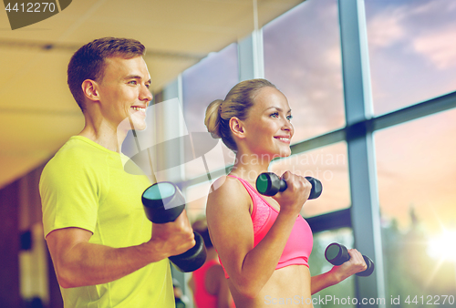 Image of smiling man and woman with dumbbells in gym