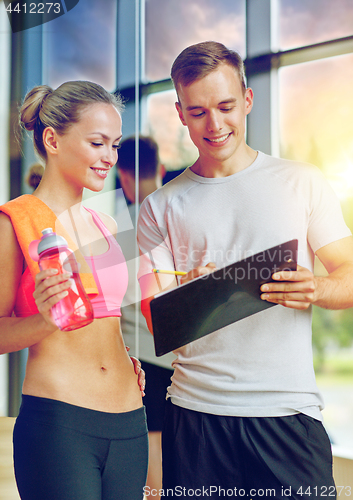 Image of smiling young woman with personal trainer in gym