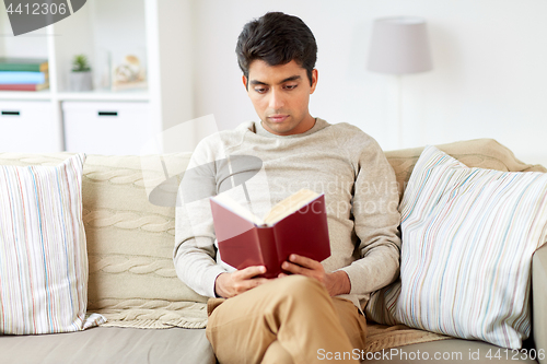 Image of man sitting on sofa and reading book at home